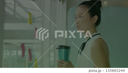 Holding mug, Asian woman wearing blouse gazing at glass office wall with sticky notes, copy space 135665244
