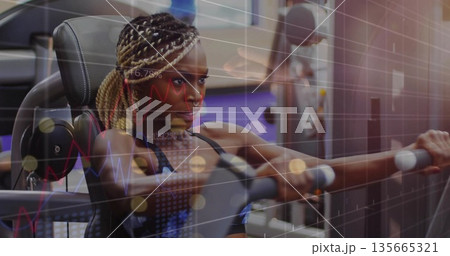 Gripping woman in sports bra pushing chest press machine at gym, with braided hair Gripping woman in sports bra pushing chest press machine at gym, with braided hair 135665321