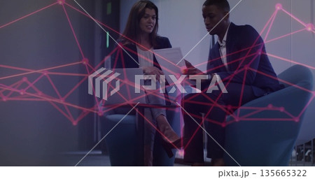 Business professionals reviewing document at round table, holding laptop in lounge with red overlay 135665322