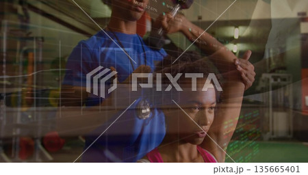 Guiding female client performing overhead arm stretching in gym weight area with rack, data overlay 135665401