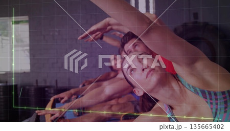 Stretching mid adult woman performing side stretch in fitness studio, with ring and brick wall 135665402