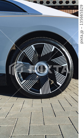 Modern car wheel with unique design displayed on paved surface near building 135665829