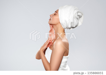 Woman with towel on head touches her neck in a wellness setting near a light background Woman with towel on head touches her neck in a wellness setting near a light background 135666031