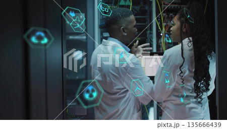 Engineers wearing lab coats analyzing server racks in datacenter, with cables and icons Engineers wearing lab coats analyzing server racks in datacenter, with cables and icons 135666439