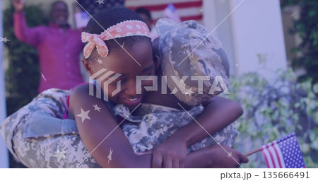 Hugging uniformed serviceman holding US flag and daughter in pink headband on porch with star decor Hugging uniformed serviceman holding US flag and daughter in pink headband on porch with star decor 135666491