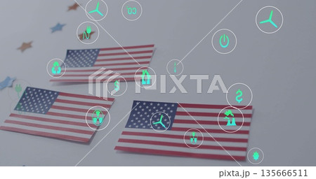 Three paper US flags displaying neon-green energy icons on light gray tabletop, with star confetti 135666511