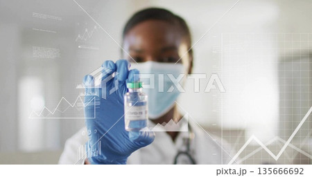 Holding researcher wearing mask and gloves analyzing chart data in hospital lab, with COVID-19 vial Holding researcher wearing mask and gloves analyzing chart data in hospital lab, with COVID-19 vial 135666692