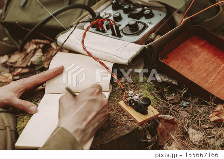 Russian Soviet Infantry Red Army Soldier In World War II using Russian Soviet Portable Radio Transceiver In Trench Entrenchment In Spring Autumn Forest. 4K. Headphones And Telegraph Key. Close Up 135667166