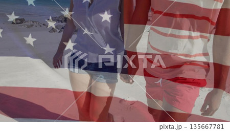 Walking couple wearing striped trunks and light blouse, shorts on sandy beach, with US flag overlay Walking couple wearing striped trunks and light blouse, shorts on sandy beach, with US flag overlay 135667781