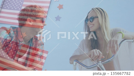 Smiling friends wearing sunglasses leaning on bike handlebars at boardwalk, with US flag overlay Smiling friends wearing sunglasses leaning on bike handlebars at boardwalk, with US flag overlay 135667782