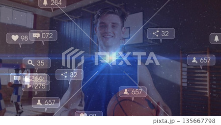 Smiling man wearing blue jersey holding orange basketball on gym court, with digital notifications Smiling man wearing blue jersey holding orange basketball on gym court, with digital notifications 135667798