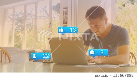 Mature man typing on silver laptop in dining workspace, with papers pen plant and social icons 135667889