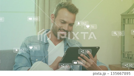 Middle-aged man smiling while holding tablet on sofa in living room with social media icons Middle-aged man smiling while holding tablet on sofa in living room with social media icons 135667895