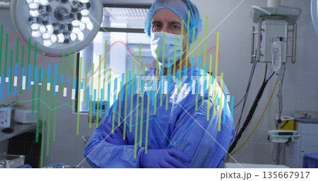 Standing surgeon in scrubs preparing surgery in operating room with surgical lights and data graphs 135667917