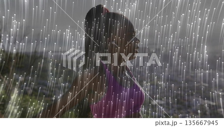 Standing Black runner wearing purple sports bra and white earphones on hillside, with rain streaks 135667945