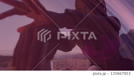 Leaning woman in pink sports bra and leggings stretching forward on rocky desert, with rock support 135667953