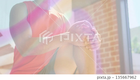 Performing fitness man holding knee-to-chest stretch in brick-walled workout area, under sunlight Performing fitness man holding knee-to-chest stretch in brick-walled workout area, under sunlight 135667962