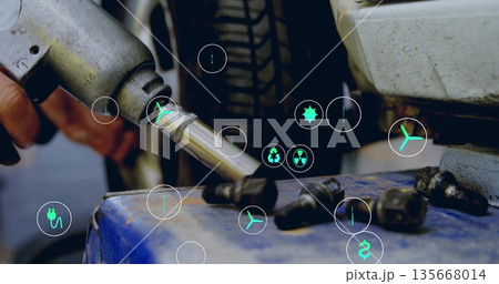 Gloved hand tightening lug nut on tire with impact wrench in workshop, energy icons, copy space 135668014