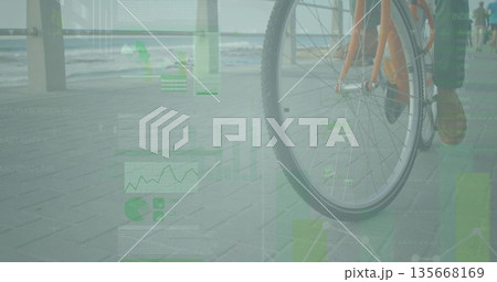 Cyclist riding seaside path past railing with orange bike wheel, green data overlay, copy space 135668169