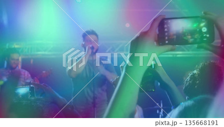 Singer singing into mic at venue under colorful truss lights, with guitarist smartphones recording Singer singing into mic at venue under colorful truss lights, with guitarist smartphones recording 135668191