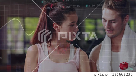 Discussing workout partners in sportswear analyzing performance data in gym, with data overlay 135668230