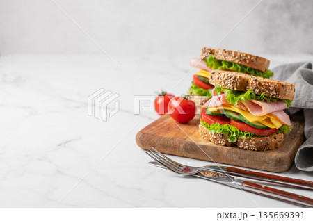 Two sandwiches with ham, cheese, lettuce, vegetables and seeded bread on a wooden board Two sandwiches with ham, cheese, lettuce, vegetables and seeded bread on a wooden board 135669391