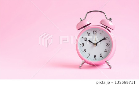 A vintage pink retro alarm clock with classic metal bells stands as a morning time reminder on a matching pink background to wake you before the deadline 135669711