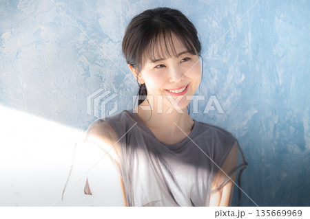 水色背景で日射しの中でポーズをとる女性　上半身笑顔　日焼け止めやuvなど紫外線のイメージ 135669969