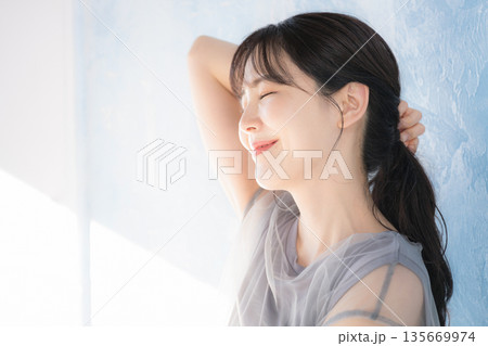 水色背景で日射しの中でポーズをとる女性の横顔　上半身 eラインのイメージ 135669974