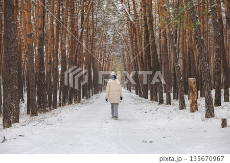 Teenage girl walking alone along snowy pine forest corridor, quiet winter path with tall trees, peaceful outdoor lifestyle, cold season travel and calm nature atmosphere 135670967