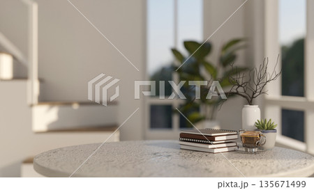 Round marble table with books and a glass of coffee aside potted plant in a modern house or building 135671499
