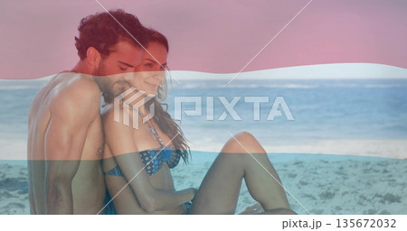 Sitting couple hugging waist on sand at water edge, wearing trunks, bikini, necklace, copy space 135672032