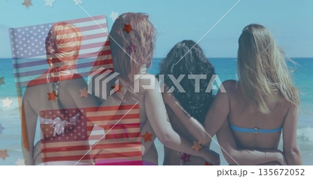 Standing four women linking arms on sandy beach by sea, with colorful bikinis, star stripe graphics 135672052