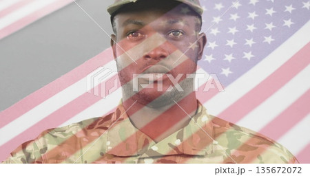 Standing male soldier wearing camouflage combat uniform and cap in grey studio, with flag overlay 135672072