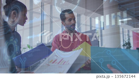 Analyzing man in red shirt interpreting printed charts at office desk, with data overlays 135672144