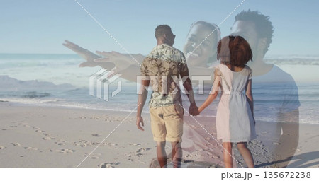 Walking couple holding hands along sandy shoreline, with footprints and gentle ocean waves 135672238