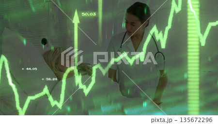 Clinician in scrubs leaning over patient on hospital bed with stethoscope and financial overlay 135672296