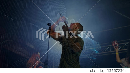 Singing lead vocalist gripping microphone on dark concert stage, with tambourine, spotlights, haze Singing lead vocalist gripping microphone on dark concert stage, with tambourine, spotlights, haze 135672344
