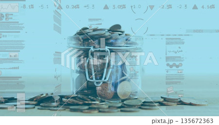 Transparent glass jar holding assorted coins on wooden surface in studio, with blue graphs 135672363