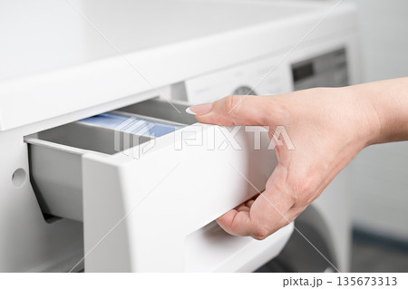 A woman's hand opens the detergent drawer in a washing machine 135673313