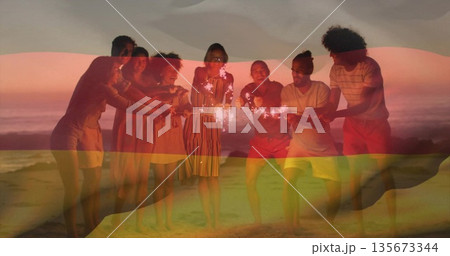 Eight friends leaning on sandy beach at sunset over ocean horizon, with handheld sparklers glowing Eight friends leaning on sandy beach at sunset over ocean horizon, with handheld sparklers glowing 135673344