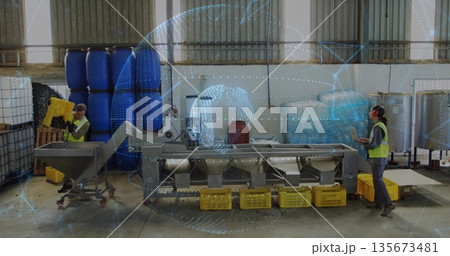 Operators monitoring tablet and lifting yellow plastic crates in warehouse, with conveyor 135673481