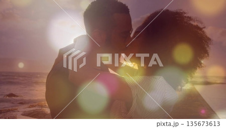 Standing romantic couple wrapping arms and leaning for kiss on wooden pier at sunset, ocean waves Standing romantic couple wrapping arms and leaning for kiss on wooden pier at sunset, ocean waves 135673613