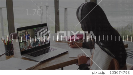 Writing student at desk by window, with headphones laptop showing videocall and notebook Writing student at desk by window, with headphones laptop showing videocall and notebook 135674798
