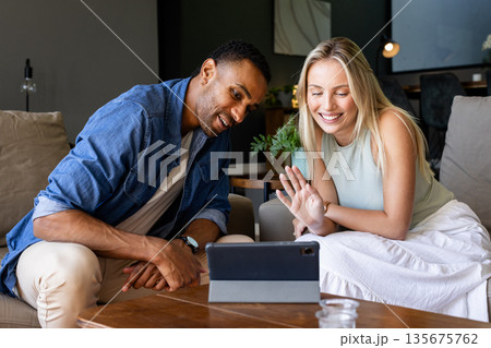 Smiling couple video chatting on tablet in cozy living room setting Smiling couple video chatting on tablet in cozy living room setting 135675762