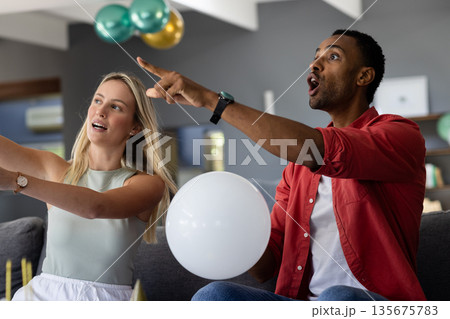 Celebrating at home, friends holding balloons and pointing excitedly together Celebrating at home, friends holding balloons and pointing excitedly together 135675783