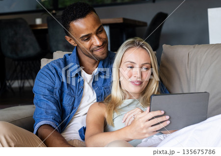 Couple relaxing on couch, enjoying tablet together at home, smiling warmly 135675786