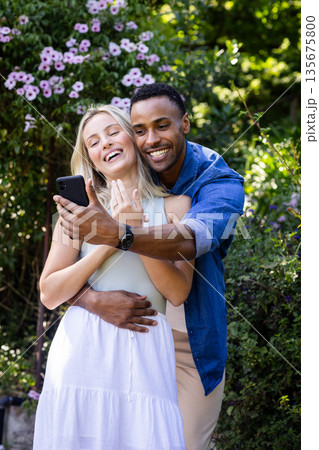 Couple celebrating engagement, smiling and taking selfie in garden with smartphone 135675800
