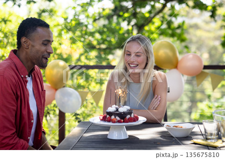 Celebrating birthday outdoors, friends with cake and balloons sharing joyful moments 135675810
