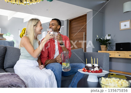 Couple celebrating at home, toasting with drinks and enjoying birthday cake 135675856